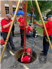 Group of Firefighters Lowering One of Their Own Into a Manhole